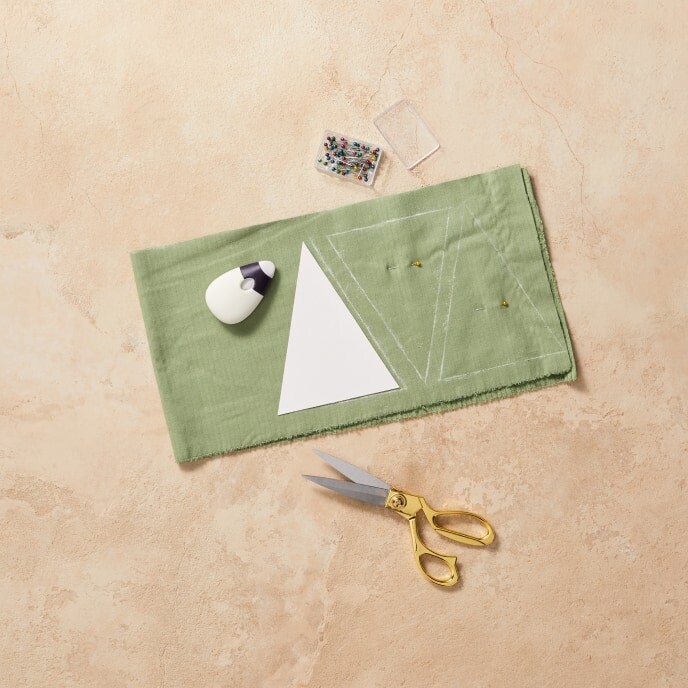 Step 2 of the tutorial: A pair of scissors cutting along the outlined shapes on patterned paper, showing the process of creating pouches for the Advent calendar.