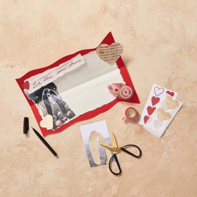Step 4: An image of an almost finished Valentine’s Day card, decorated with photos, handwritten messages, and embellishments, attached to a "merci" chocolate pack using double-sided tape.